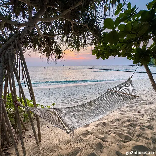 Colorful hammock tied between palm trees overlooking Bang Tao Beach sand and Andaman Sea in Phuket, Thailand