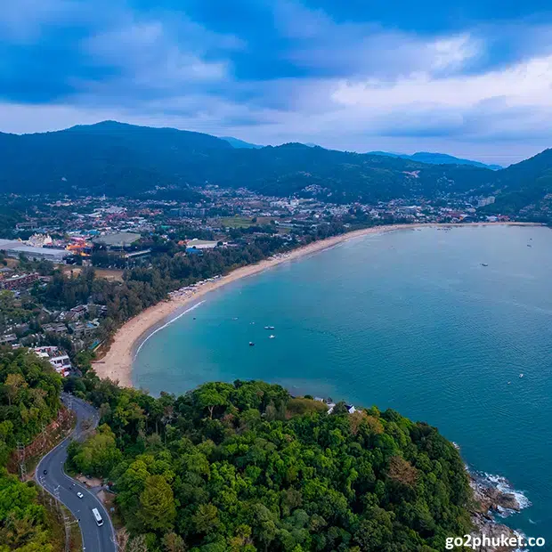 Aerial view of Kamala Beach coastline with turquoise water, sandy shore, and tropical hills in Phuket Thailand.
