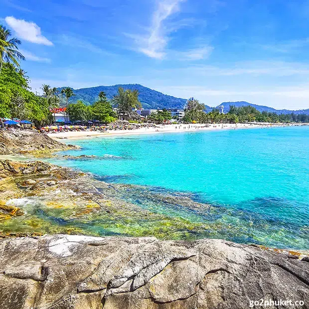 Rocky point with waves meeting sand and tropical coastline at Kamala Beach, Phuket, Thailand.