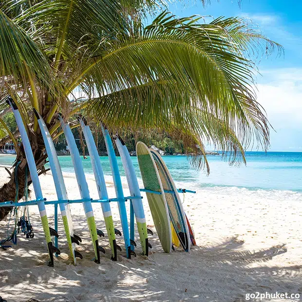 Colorful surfboards standing on sandy Kata Beach with Andaman Sea waves in Phuket Thailand