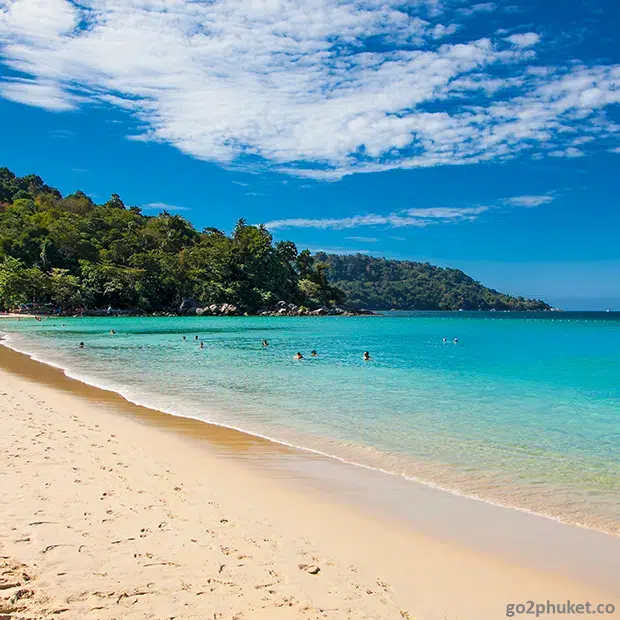 Beachgoers swimming and relaxing in clear Andaman Sea water at Kata Beach in Phuket Thailand
