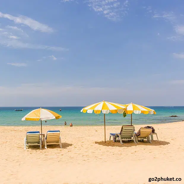 Rows of beach deck chairs and umbrellas on sandy Kata Beach beside turquoise Andaman Sea in Phuket Thailand