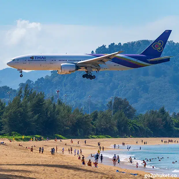 Passenger airplane flying low over Mai Khao Beach during landing approach in Phuket, Thailand