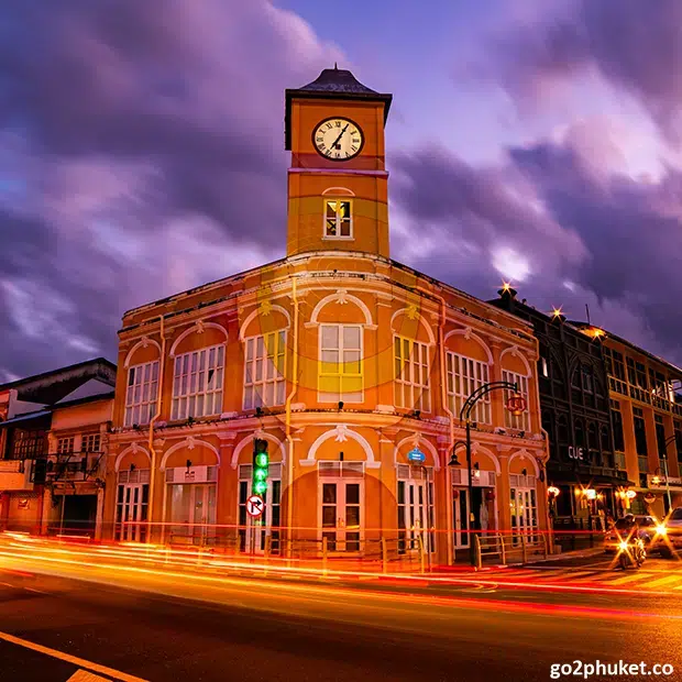 Colorful Sino-Portuguese buildings and lanterns along a lively street in Phuket Old Town during early evening.