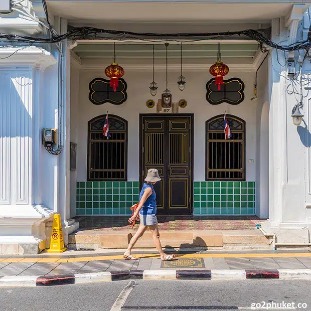 Woman walking past colorful Sino-Portuguese buildings along a historic street in Phuket Old Town, Thailand.