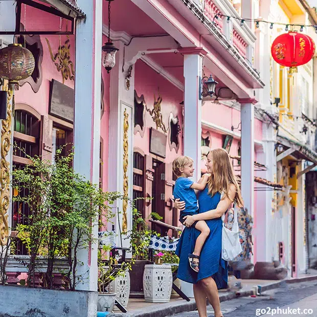 Mother and child walking along colorful historic street lined with Sino-Portuguese buildings in Phuket Old Town Thailand.