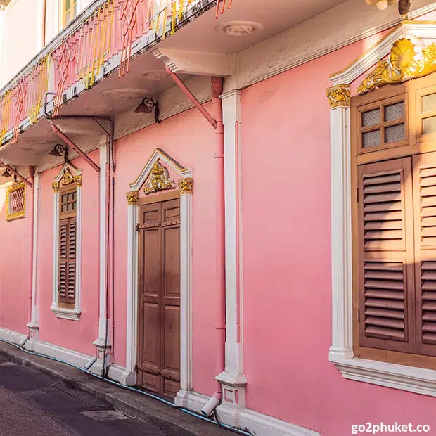 Pink Sino-Portuguese heritage building with arched windows along a historic street in Phuket Old Town Thailand.