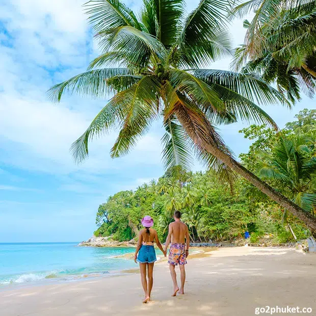 Man and woman walking hand in hand along Surin Beach shoreline beside the Andaman Sea in Phuket, Thailand