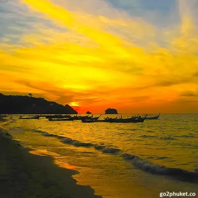 Traditional fishing boats on Nai Yang Beach with golden sunset over the Andaman Sea in Phuket Thailand